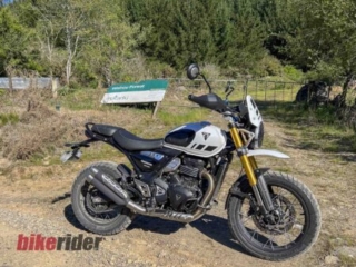 Triumph Scrambler 400XC parked on gravel road by forest