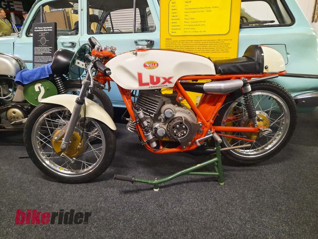 Museum display of vintage motorcycles with a mint-green classic car in the background