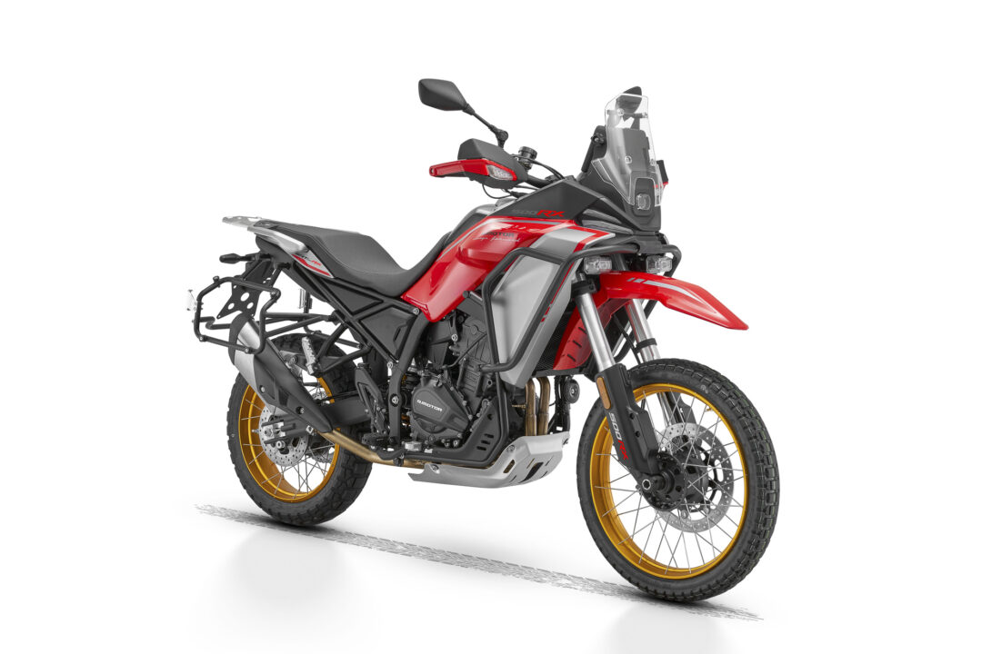 Red adventure motorcycle shown in side profile with a tall windshield and gold-rimmed wheels on a white background.
