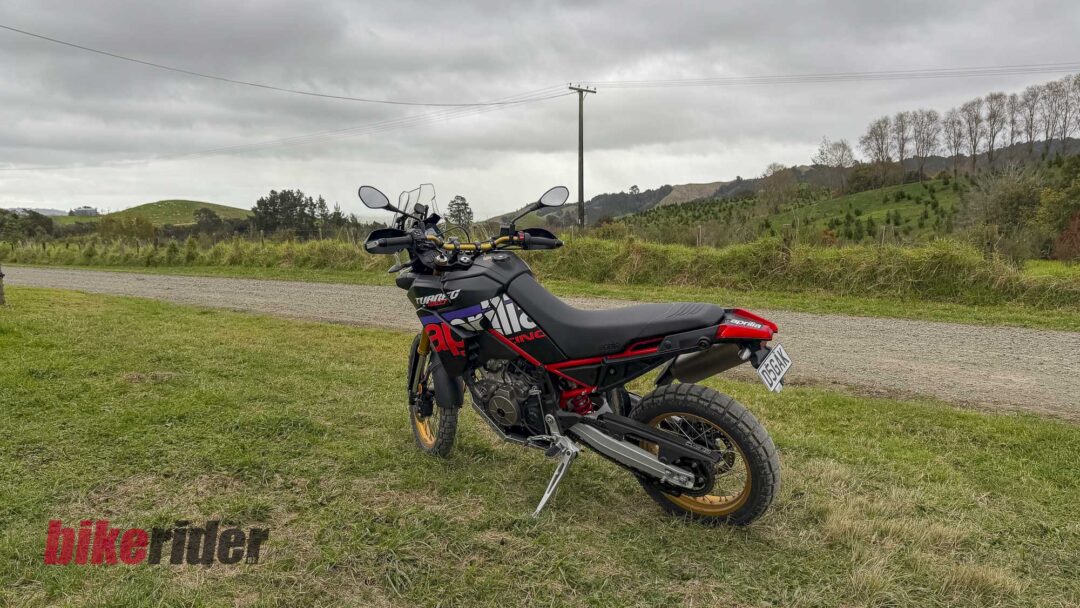 Sport motorcycle parked on grass with a cloudy sky and rural hills in the background; red and black graphics on the bike.