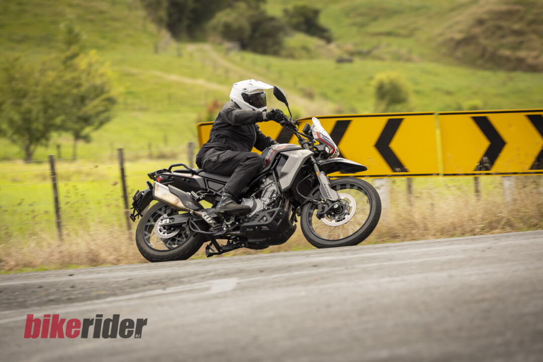 Motorcyclist in protective gear leaning into a turn on a rural road beside a yellow and black chevron barrier.