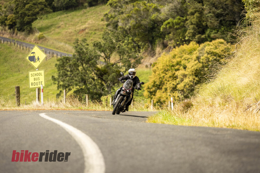 Motorcyclist wearing a white helmet rides a curving rural road beside a yellow 'School Bus Route' sign.