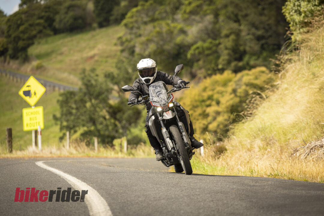 Motorcyclist wearing white helmet riding a black motorcycle around a sweeping road bend, countryside in the background