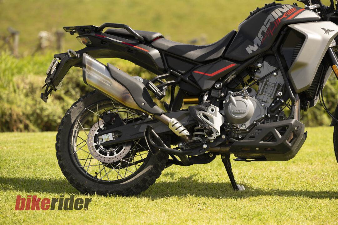 Close-up of a black sport-adventure motorcycle on grass, showing rear wheel, exhaust, and engine.