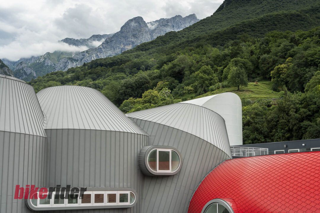 Sleek, ribbed metal domes of a modern building set against a forested hillside and misty mountain range in the background.