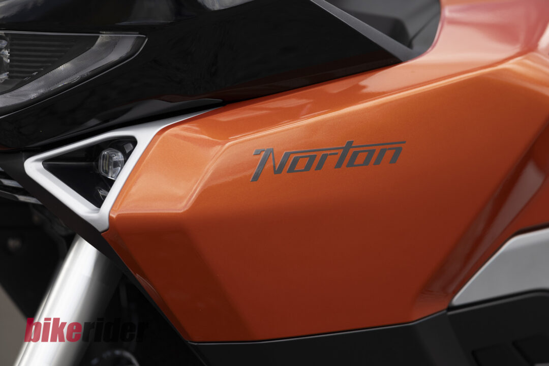 20260703-Norton_Atlas_2026_Details26-1080x720 Close-up of an orange motorcycle fairing with a black windshield and part of the headlight visible