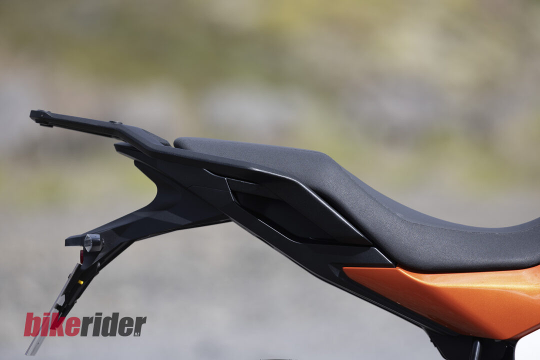 20260703-Norton_Atlas_2026_Details7-1080x720 Close-up of a motorcycle rear seat and tail, black textured surface with orange lower fairing and 'bikerider.nz' watermark in the corner.