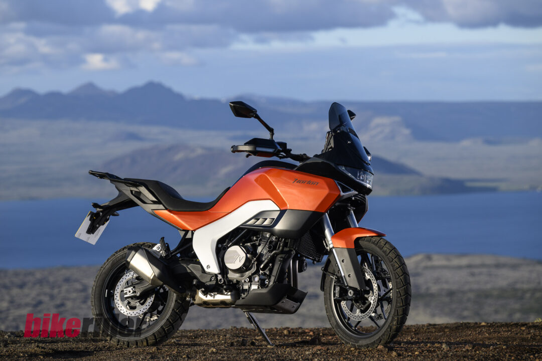 20260703-Norton_Atlas_2026_Offroad_Statics16-1080x720 Orange adventure motorcycle parked on a dirt road with a mountainous landscape in the distance.