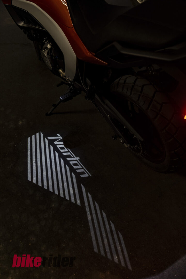 Close-up of a motorcycle's rear side with kickstand down in a dark setting; red bodywork and large tire visible, ground logo partially showing.