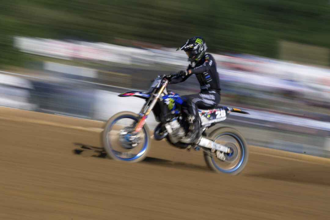 Motocross rider in black gear on a blue dirt bike speeding along a dirt track with motion blur in the background.