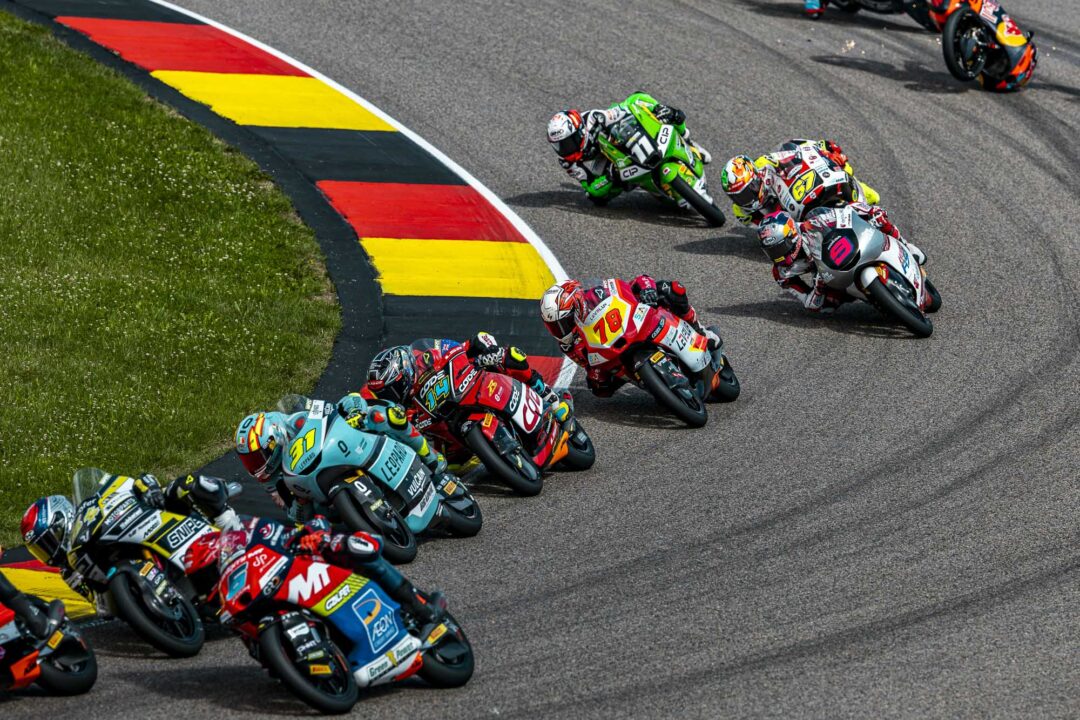 Group of riders in colorful racing suits leaning into a sharp turn on a track.