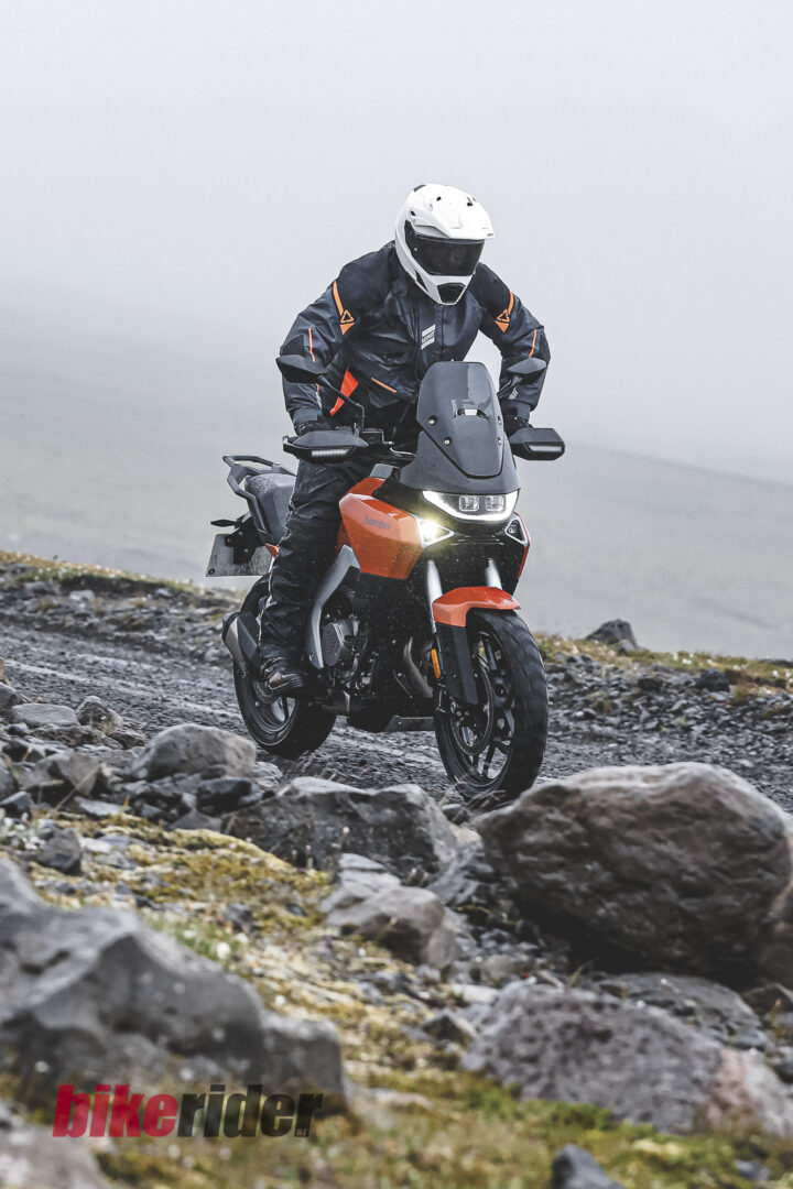20260712-Norton-Atlas-Global_B_19313-28-720x1080 Motorcyclist in a white helmet on an orange adventure bike navigating a rocky coastal trail.