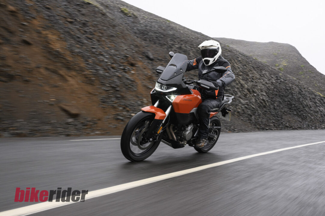 Motorcyclist wearing helmet and protective gear on a red adventure bike leaning into a turn on a winding road beside a rocky hillside