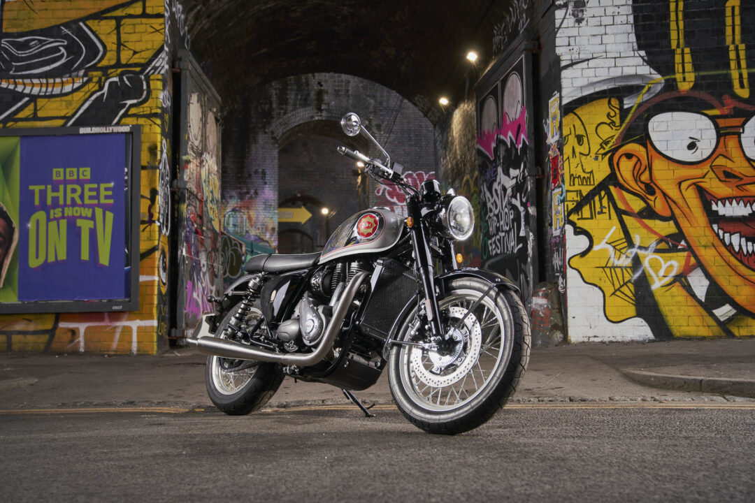 Motorcycle parked in a graffiti-covered alley with brick arches, facing the camera at a slight angle.