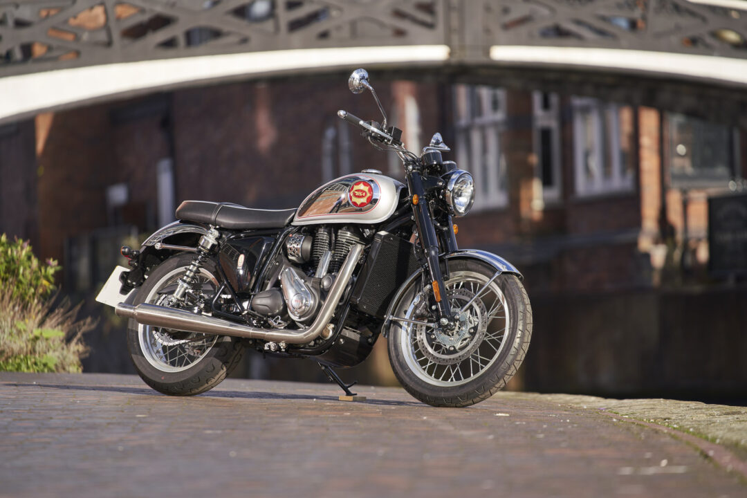 Classic motorcycle in black and chrome on a brick-paved street with a blurred brick building in the background.