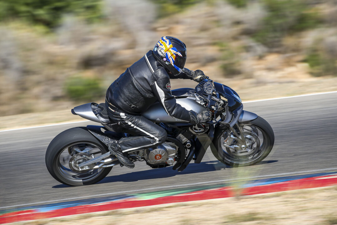 Motorcyclist in black leather gear leaning into a turn on a race track, helmet with colorful design