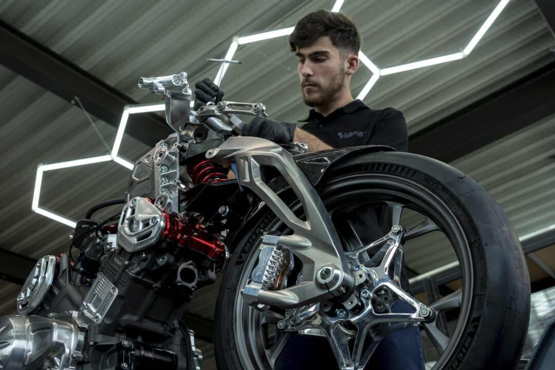 A young man in gloves works on a high-tech motorcycle frame in a bright workshop.