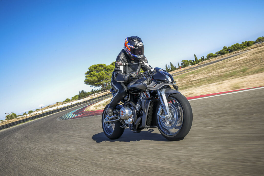 Brough-superior-rmb-01-12 Motorcycle rider in full protective gear leans into a curve on a race track beneath a clear blue sky