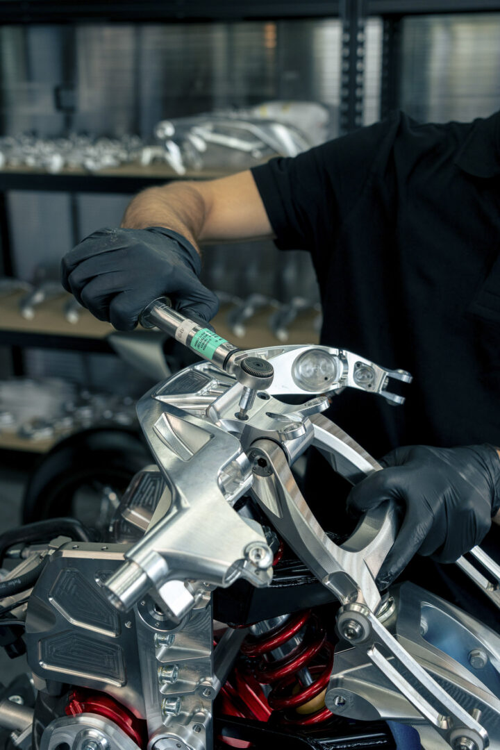 Brough-superior-rmb-01-13 Technician in black gloves tightening a bolt on a shiny motorcycle frame with a torque wrench in a workshop.