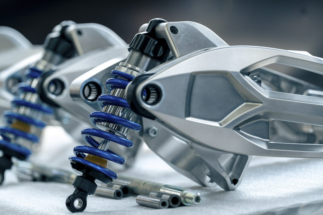 Brough-superior-rmb-01-16 Close-up of a car suspension with blue coil springs and chrome shock absorber components.