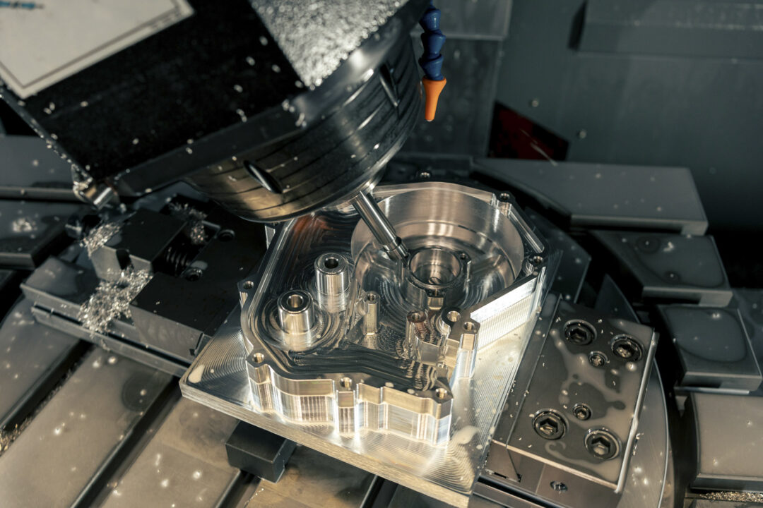 CNC milling center shaping a metal fixture with a rotating spindle and orange coolant nozzle nearby, metallic chips scattered around.