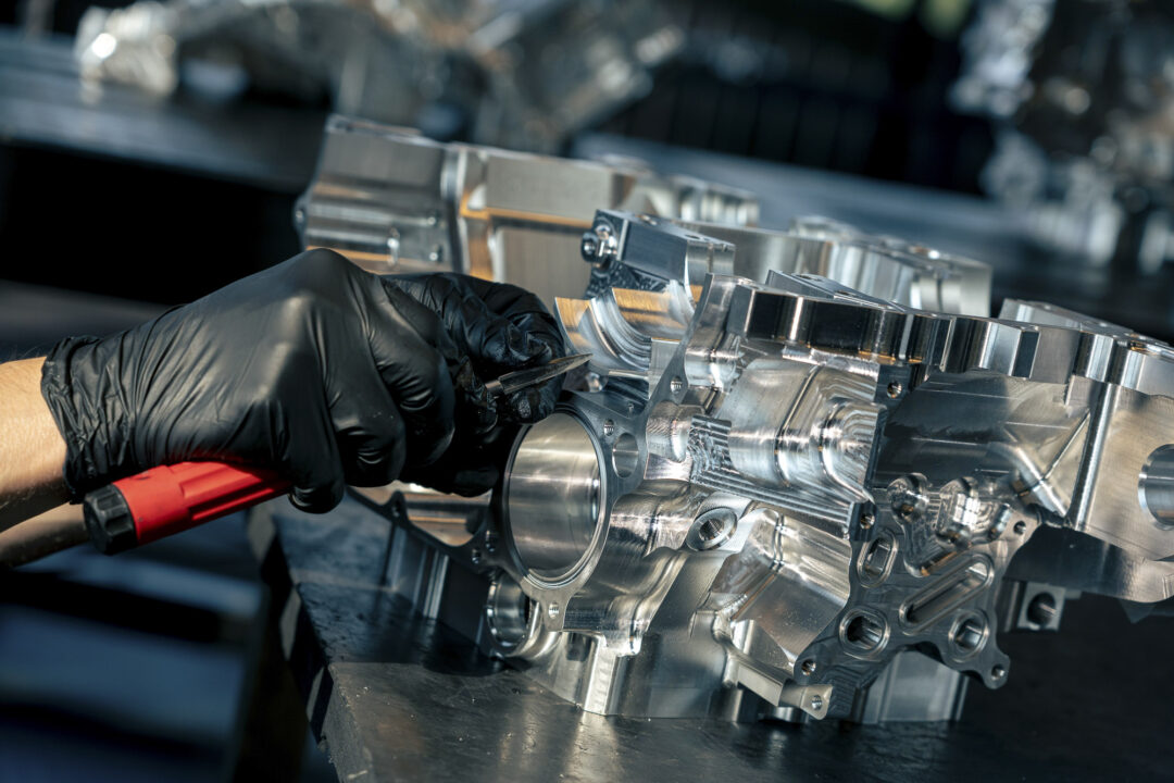 Technician in black gloves tooling a polished metal machine component in a workshop.