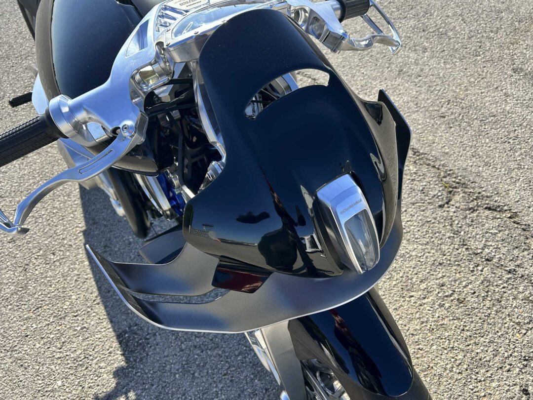 Brough-superior-rmb-01-2-2 Close-up of a glossy black motorcycle front fairing with chrome handlebars and chrome trim, parked on pavement