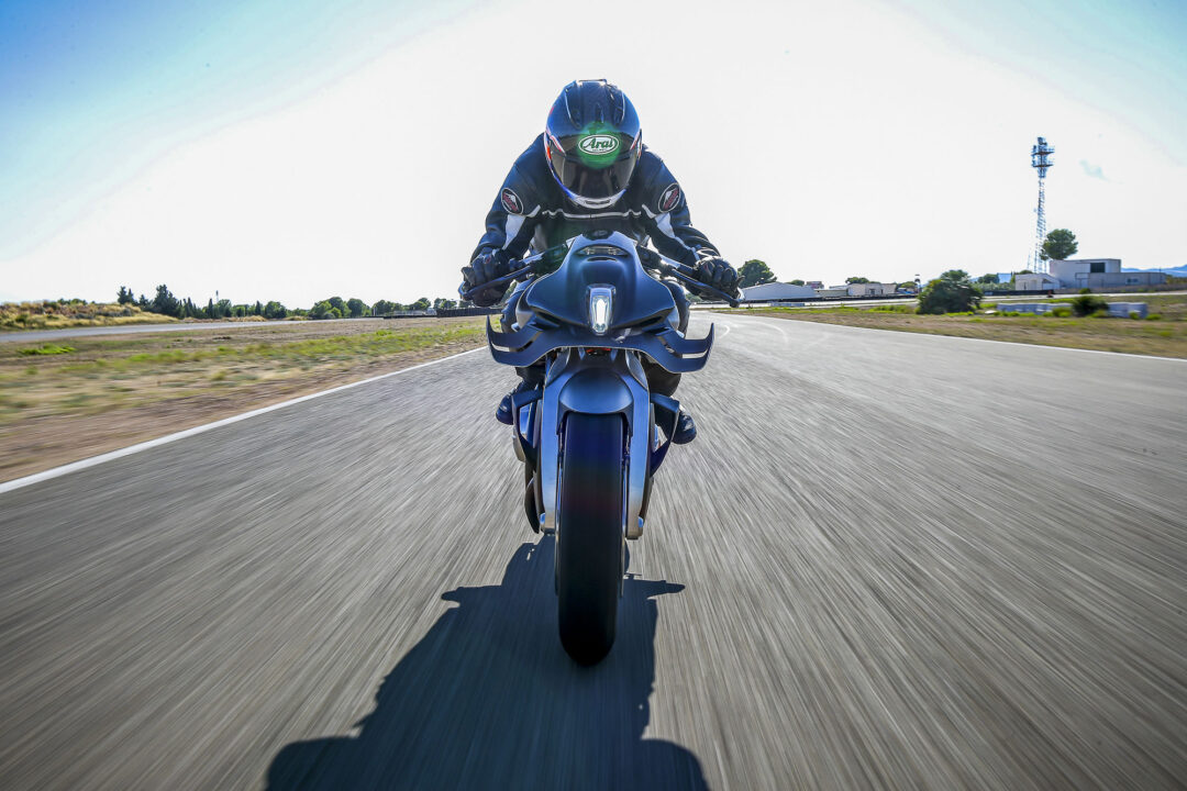 Motorcyclist wearing a blue helmet and suit leaning forward on a blue sport bike on an open road