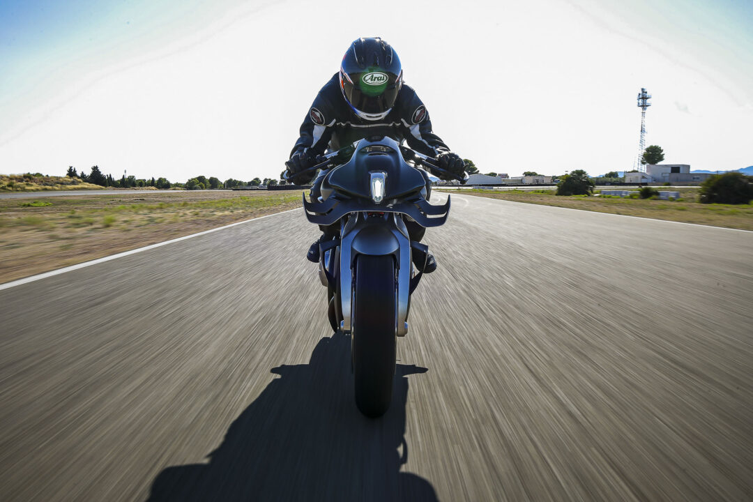 Brough-superior-rmb-01-6 Rider in full gear on a blue sport motorcycle, shot from behind and low to the road as they speed down a straight highway.