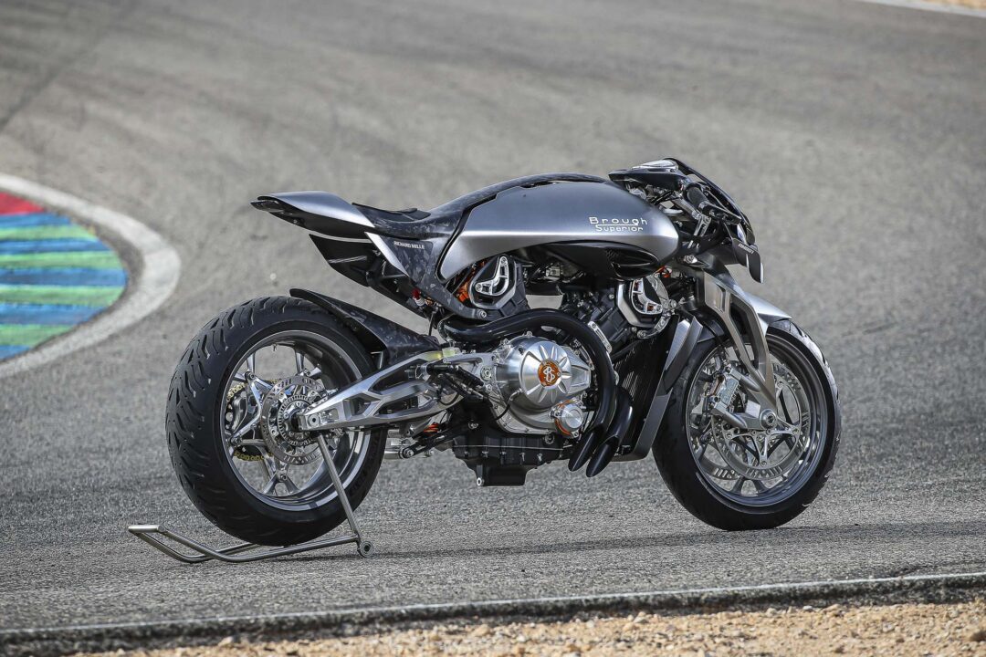 Brough-superior-rmb-01-6-2 A metallic gray Brough Superior motorcycle on a race track with its kickstand down, rear wheel visible on asphalt.