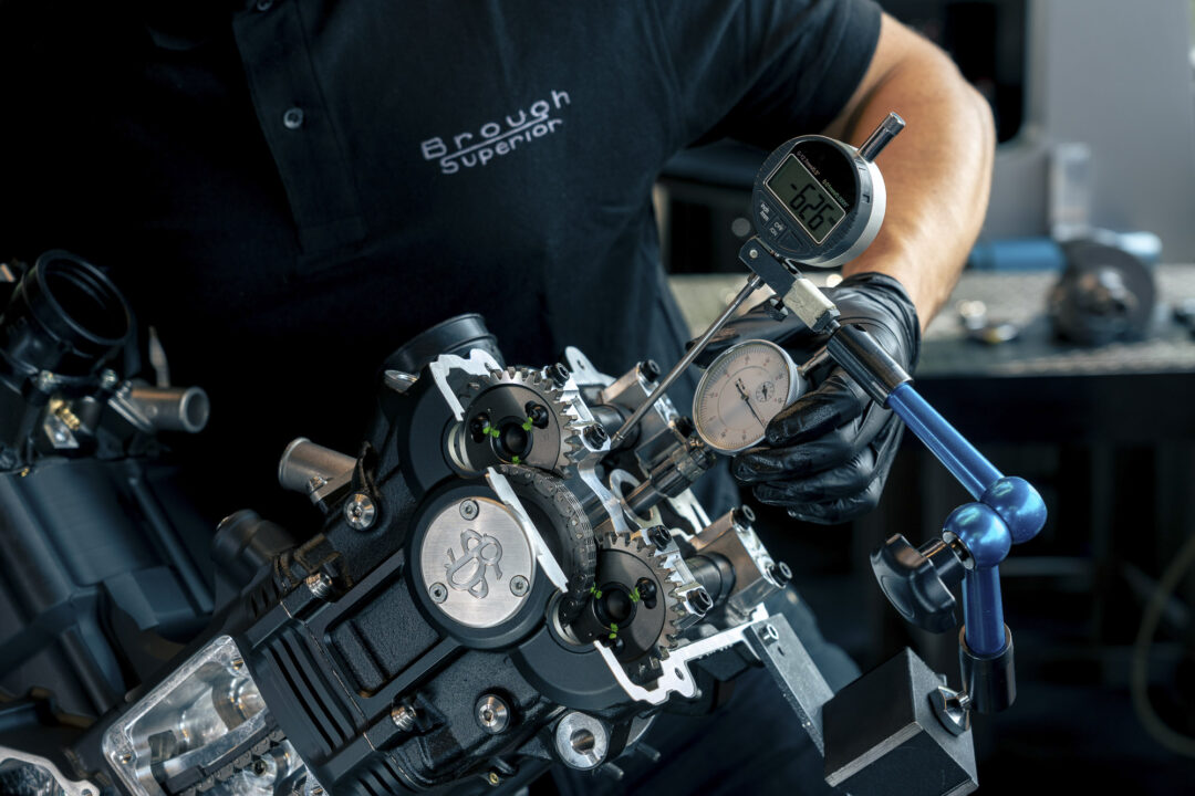 Brough-superior-rmb-01-8-1 Technician in gloves using a dial gauge to measure a gear assembly in a workshop.