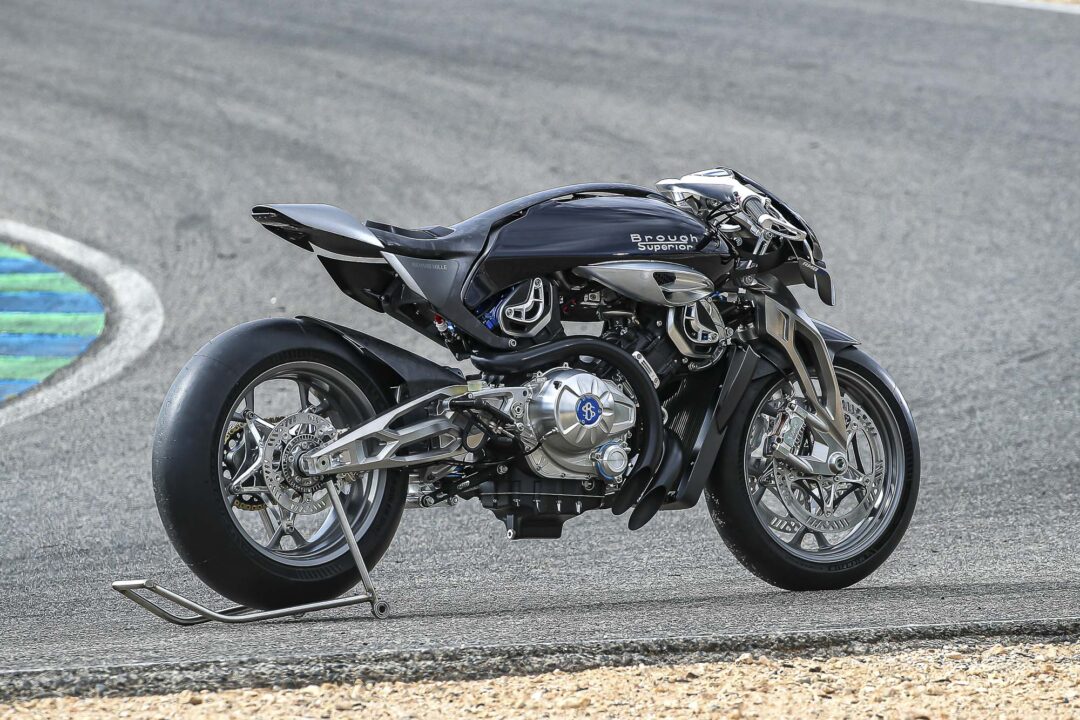 Brough-superior-rmb-01-8-2 Black Brough Superior motorcycle on a race track, supported by a metal stand near a curbed corner.