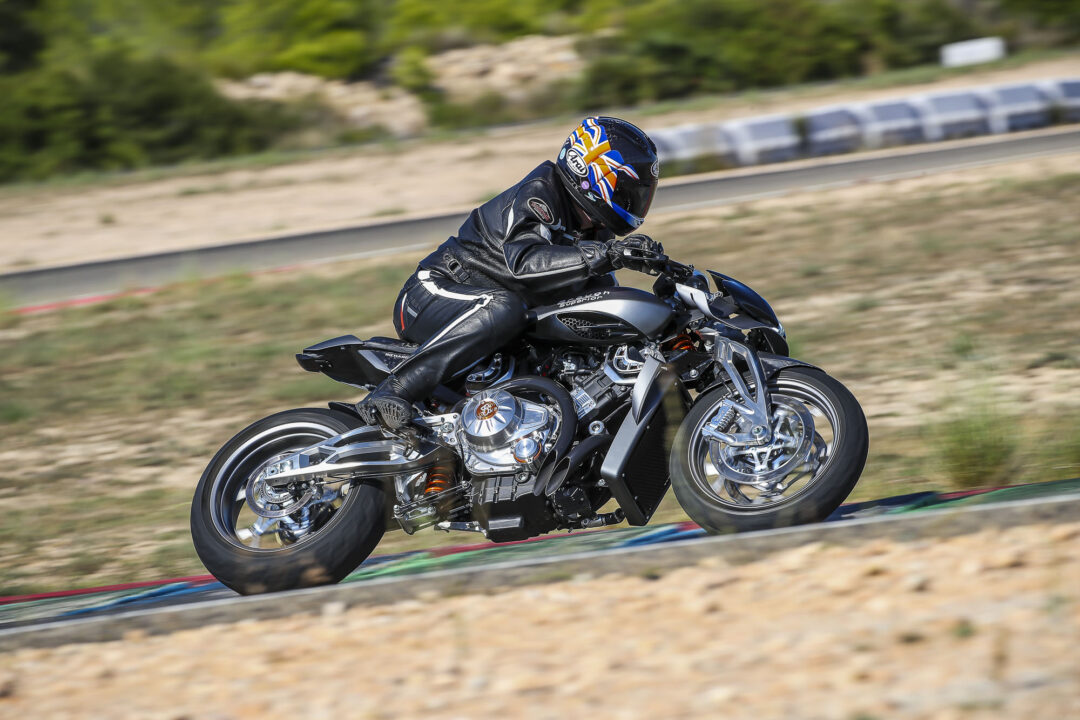 Motorcyclist in black leather gear leaning into a curve on a race track, helmet with blue and orange design