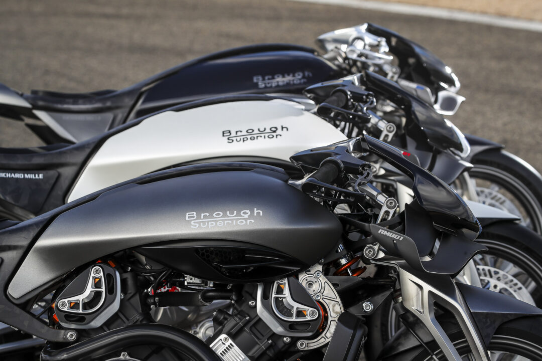 Brough-superior-rmb-01-9-2 Row of black and silver Brough Superior motorcycles parked side by side, close-up of the fuel tanks with branding visible.