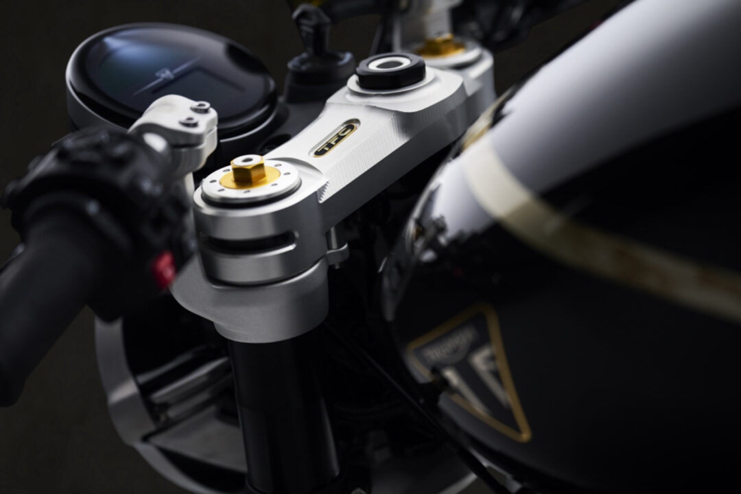 Close-up of a motorcycle front suspension with adjustable fork caps and a blurred instrument panel in the background.
