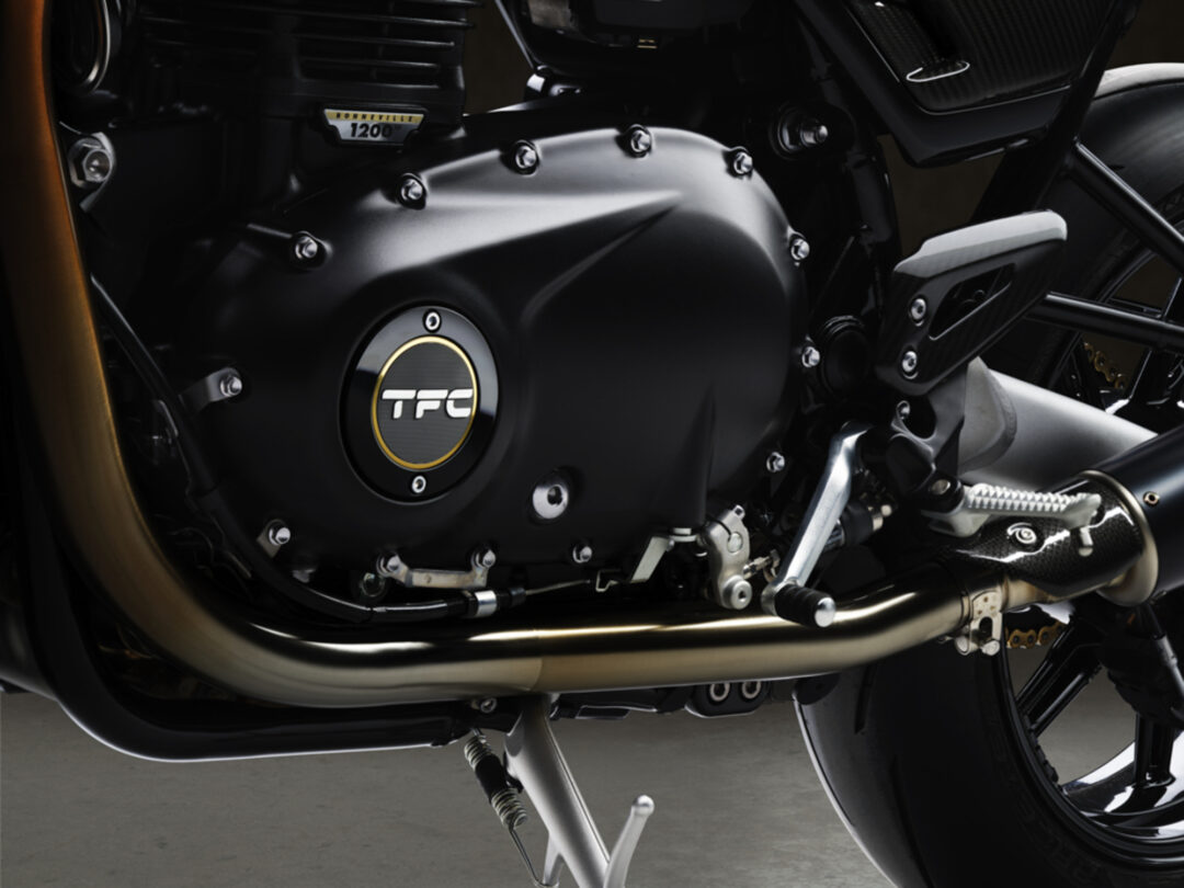 Close-up of a black motorcycle engine with chrome bolts and a circular TFC badge on the cover.