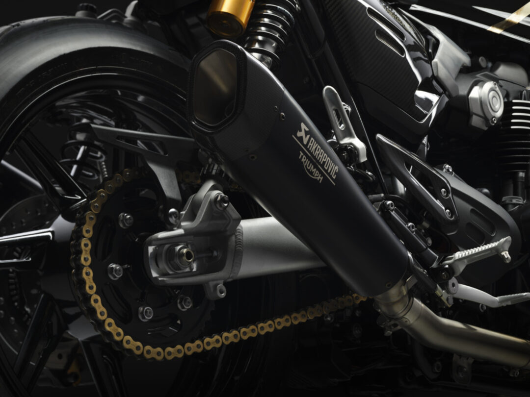 Close-up of a black motorcycle rear section, showing the gold chain, exhaust, and suspension components.
