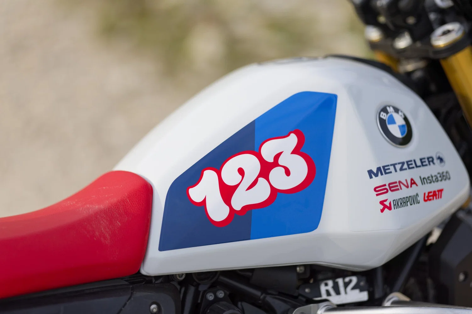 Close-up of a white racing motorcycle fuel tank with a blue 123 decal and BMW logo.