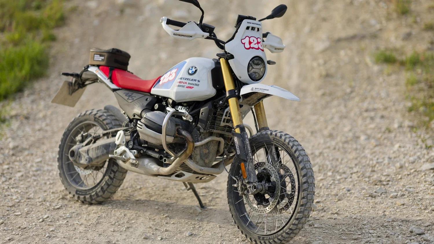 Off-road BMW dirt bike parked on a rocky gravel trail, white body with red seat and a large number plate reading 126/A.”