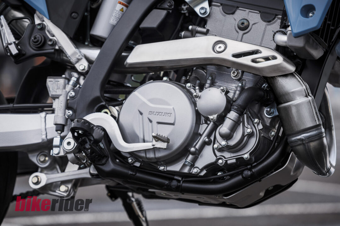Close-up of a Suzuki motorcycle engine and surrounding frame with metal components and bolts visible.