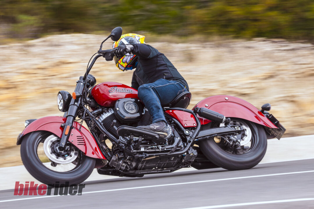 Motorcyclist in colorful helmet leaned into a red Indian motorcycle riding at speed on a highway with a blurred background