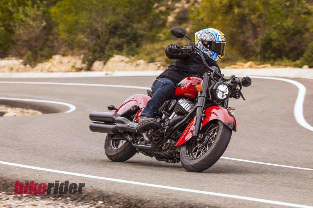Motorcyclist wearing a colorful helmet leans into a right-hand turn on a red motorcycle.