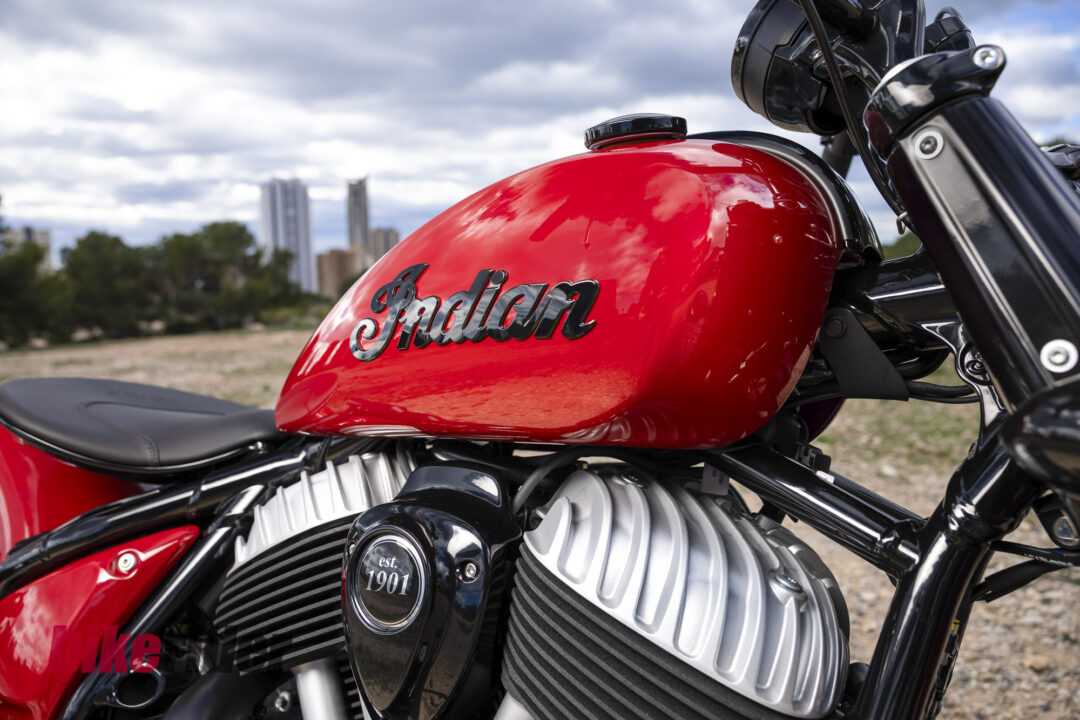 Close-up of a glossy red Indian motorcycle fuel tank with chrome badge and engine fins in the foreground