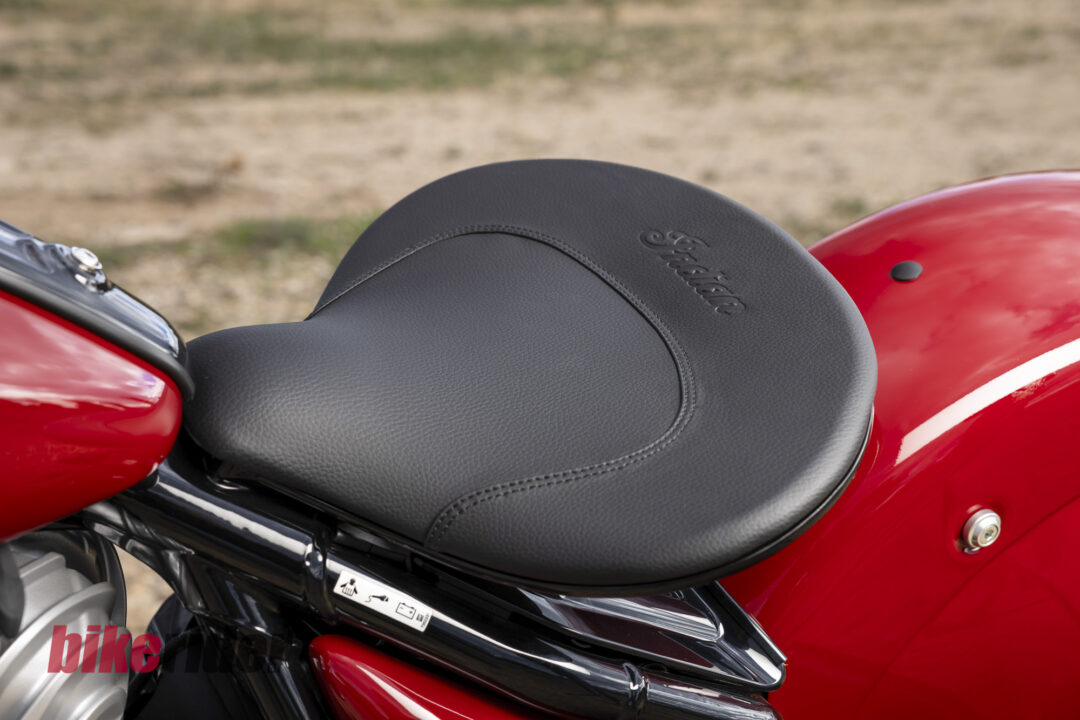 Close-up of a black textured motorcycle seat on a glossy red bike, showing a stitched seam and embossed branding.