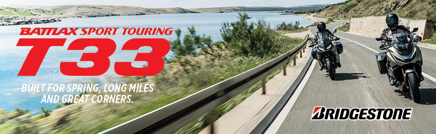 Bridgestone T33 ad: two motorcyclists ride along a coastal highway; bold red T33 text with the slogan 'Built for spring, long miles and great corners'