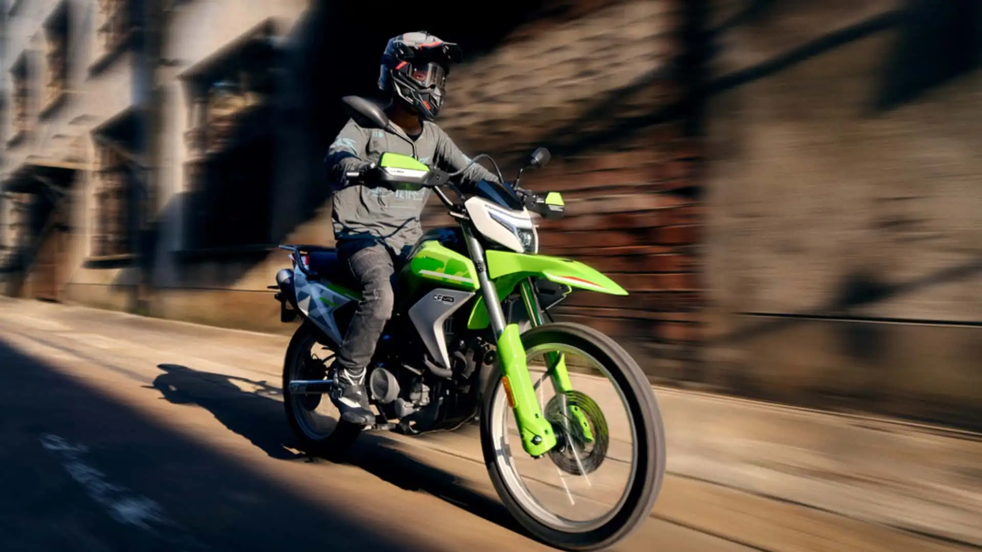 Motorcyclist wearing a full-face helmet rides a bright green motorcycle along a city street.