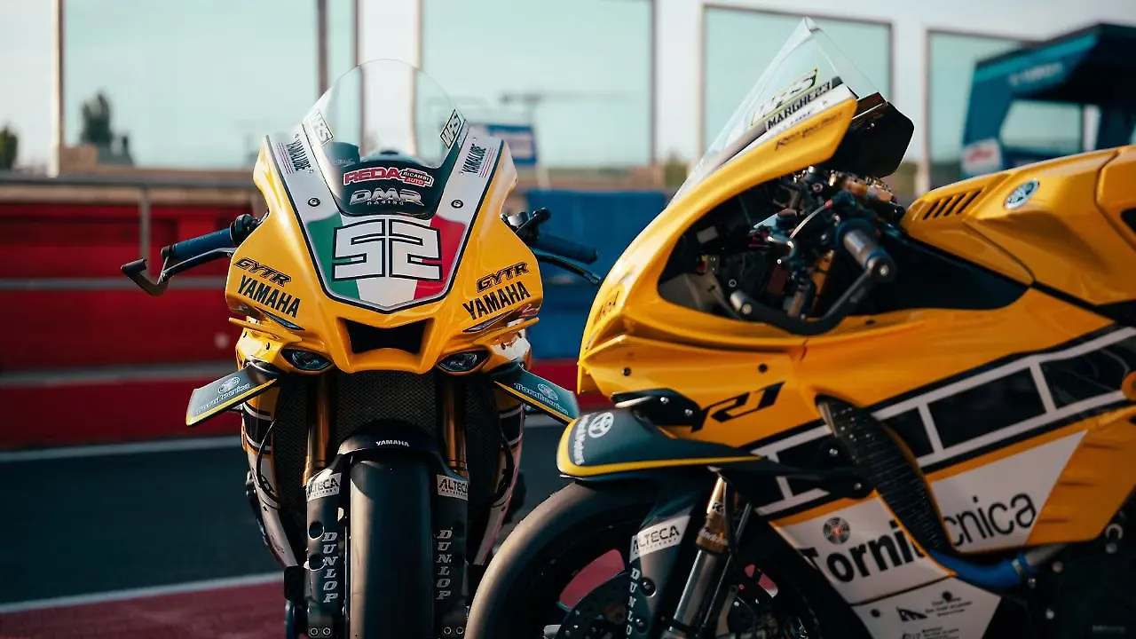 Two yellow Yamaha racing motorcycles parked side by side in a pit lane, the front bike showing the number 52 and Italian colors on its fairing.