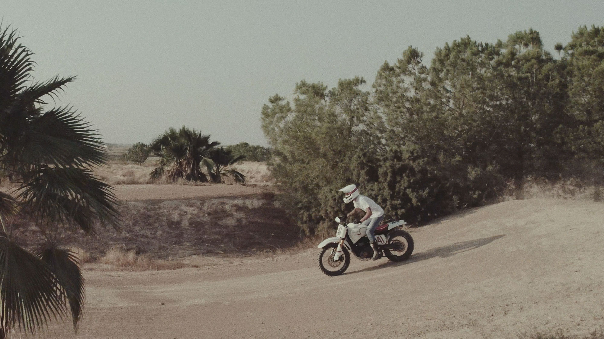 Tamarit’s Scrambler 400 XC being ridden along a dirt track beside trees
