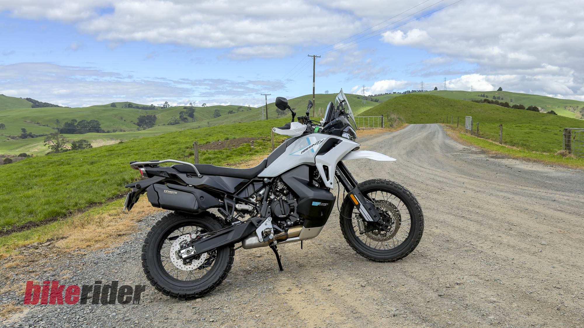 CFMOTO 1000MT-X adventure bike in side profile beside a rural gravel road