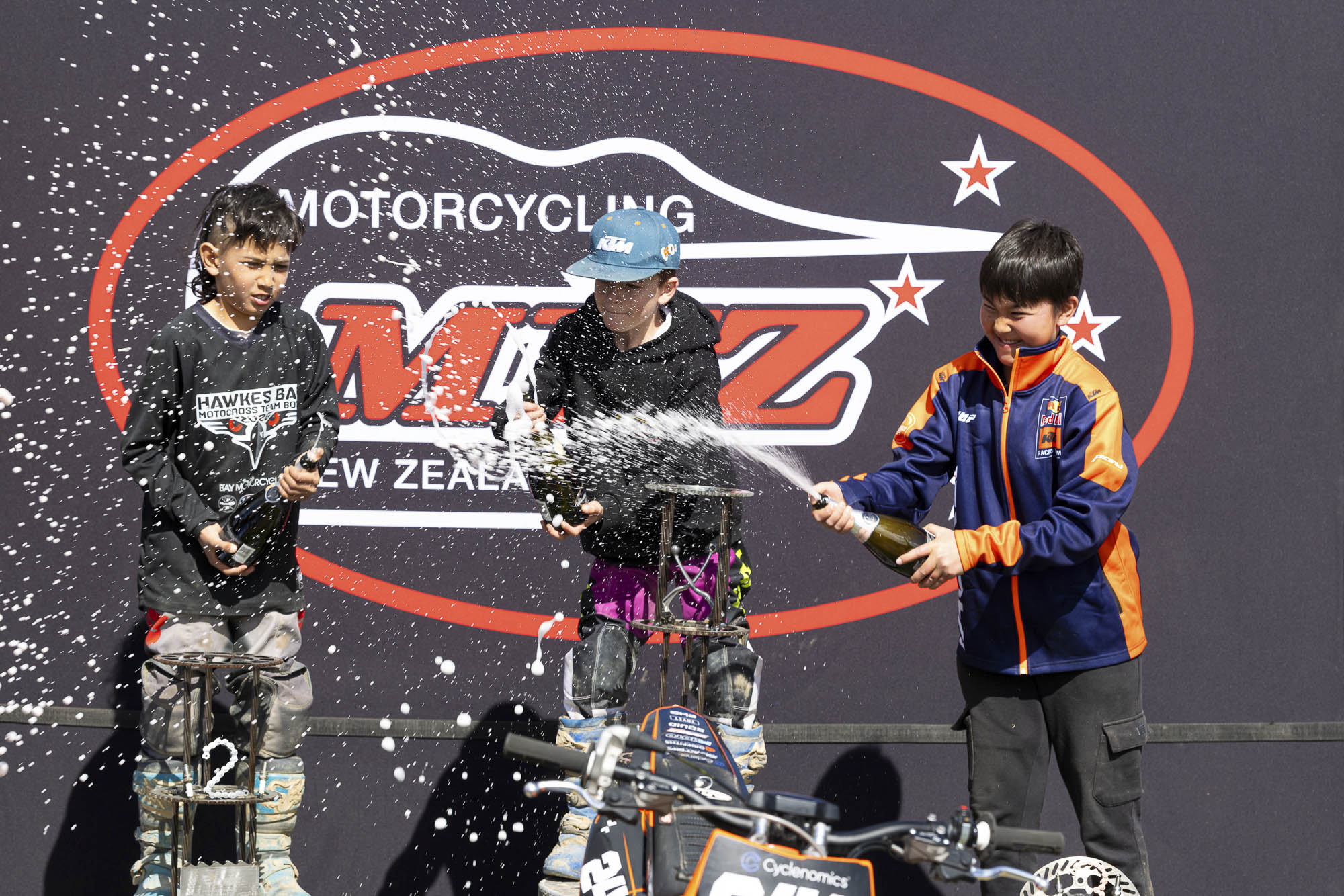 20261004-20261004_MiniMX_3557 The MX65 9-11 Years class podium celebrates with champagne (sparkling grape juice), from left: Dante McConnell (2nd), Royce Bush (1st) and Anand Rothe (3rd) at the 2026 NZ Mini Motocross Nationals